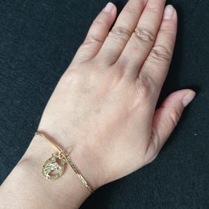 May include: A gold-toned bracelet featuring a textured chain and a single horseshoe-shaped charm. The charm has a detailed, embossed surface and is attached to the bracelet with a small circular jump ring, creating a simple and classic jewellery piece.