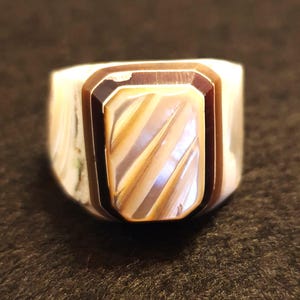 May include: A rectangular ring with a mother-of-pearl centre and a brown border. The ring has a white band with a marbled effect. The ring is a statement piece.