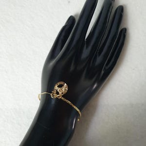 May include: A thin gold-toned bracelet featuring a textured, shimmering chain and a small, circular gold-toned charm with an embossed horseshoe design. The bracelet is delicate, with a polished finish that reflects light across its surface.