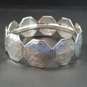 May include: Silver bracelet with a series of octagonal links. Each link is engraved with a rider on horseback. The bracelet has a classic design, suitable for everyday wear or special occasions. The circumference is approximately 18 cm.