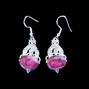 Peut inclure: Une paire de boucles d'oreilles pendantes en argent avec des pierres ovales facettées rose foncé serties dans un travail de métal filigrané orné. Chaque boucle pend à un crochet en argent et présente des détails perlés autour de la pierre.