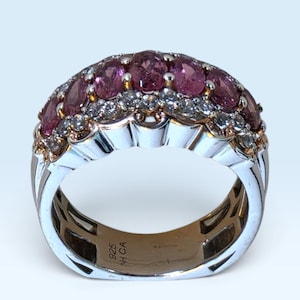 May include: A sterling silver ring featuring a row of oval-cut pink gemstones accented by a row of small clear round stones. The interior of the band is stamped with the text 925 NH CA, indicating the metal composition and maker's mark.