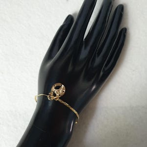 May include: A gold-toned bracelet featuring a textured, thin band and a single charm shaped like a horseshoe with a central horse head design. The metal charm is attached to the bracelet with a small jump ring, creating a simple, metallic accessory.