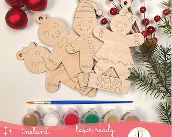 May include: A DIY gingerbread man ornament kit with wooden cutouts, paint pots, and a paintbrush. The kit includes gingerbread man and woman shapes, a bow-shaped ornament, and a nameplate that says "REVA". The image also includes red Christmas ornaments and greenery.