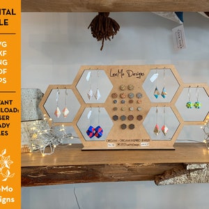 Peut inclure: Un présentoir en bois en forme de nid d'abeille, présentant des boucles d'oreilles inspirées de l'origami. Le présentoir porte l'inscription "LeeMo Designs" et "Instant Download: Laser Ready Files". Les boucles d'oreilles sont de couleurs et de motifs variés.