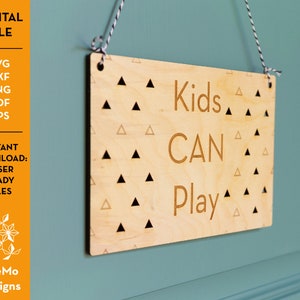 Könnte beinhalten: Ein Holzschild mit hellbraunem Hintergrund und schwarzem Dreiecksmuster. Das Schild trägt die Aufschrift "Kids CAN Play" in schwarzer Schrift.
