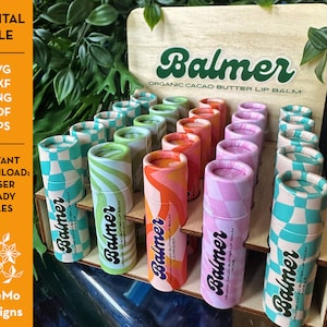 May include: A wooden display stand with multiple rows of colorful lip balm tubes. Each tube has a different pattern and says "Balmer Organic Cacao Butter Lip Balm".