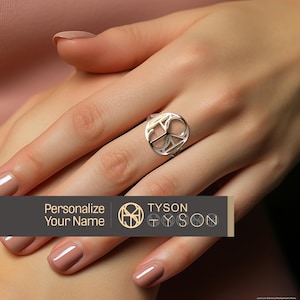 May include: A silver ring featuring a peace sign design. The ring is worn on a person's finger. The text "Personalize Your Name" and "TYSON" is visible in the image.