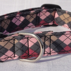 May include: A pink, gray, and brown argyle patterned dog collar with a black plastic buckle and a silver metal D-ring.