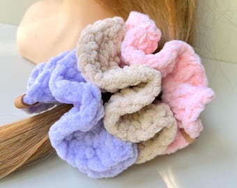 May include: A multi-colored hair scrunchie made of soft, plush, textured yarn. The accessory features three distinct sections in light purple, beige, and soft pink, gathered together to form a ruffled, circular shape with a visible elastic band.