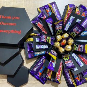 May include: A black hexagonal gift box with red text reading "Thank you Gurnam for everything." The box opens to reveal an explosion of various chocolate bars and candies, including Dairy Milk, Crunchie, and Freddo.