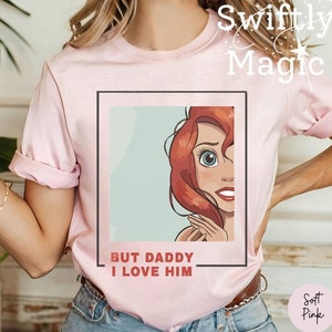 May include: Pink t-shirt with a cartoon image of a red-haired woman with the text "But Daddy I Love Him" in a white box.