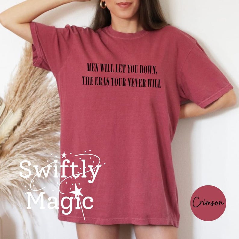 May include: Crimson-colored t-shirt with the text "MEN WILL LET YOU DOWN. THE ERAS TOUR NEVER WILL" in black. The shirt also features the text "Swiftly Magic" in white with a star design. A crimson circle with the word "Crimson" is in the lower right.