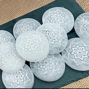 Può includere: Un set di otto sottobicchieri in selenite bianca con intricati disegni di mandala incisi sulla superficie.
