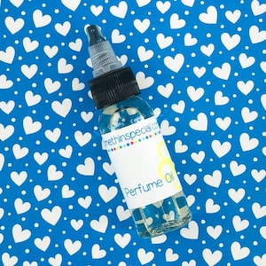 May include: A clear glass bottle with a black cap and a white label that says "Perfume Oil" and "somethingspecial.com". The bottle is sitting on a blue background with white hearts.