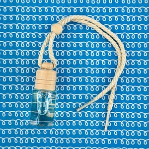 May include: A clear glass bottle with a wooden cap and a light blue liquid inside. The bottle is attached to a white string with a wooden bead at the top. The bottle is on a blue and white patterned background.