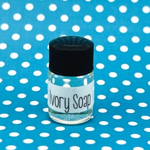 May include: A small clear glass bottle with a black lid and a white label that reads "Ivory Soap". The bottle is sitting on a blue and white polka dot background.