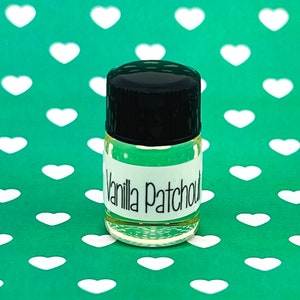 May include: A small clear glass bottle with a black lid and a white label that reads "Vanilla Patchouli". The bottle is sitting on a green background with white hearts.