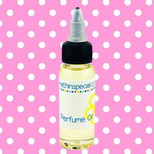 May include: A clear glass bottle of perfume oil with a black cap and a white label. The label reads "Perfume Oil" in a script font. The background is a pink polka dot pattern.