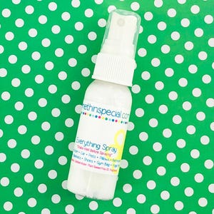 May include: A white spray bottle with a white label that says "Everything Spray" and "Shake Well Before Spraying". The label also lists a variety of items that the spray can be used on, including "Pan, Car, Pets, Pillows, Bedding, Blankets, Shoes, Gym Bag, Yoga Mat". The bottle is sitting on a green background with white polka dots.