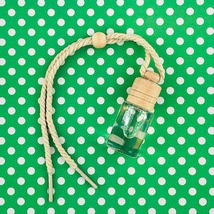 May include: A clear glass bottle with a wooden cap and a beige string hanging from it. The bottle is filled with a light green liquid. The bottle is hanging on a green background with white polka dots.