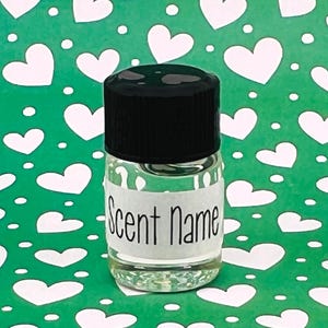 May include: A small, clear glass bottle with a black cap. The bottle has a white label with the words "Scent Name" printed on it. The background is green with white heart shapes.