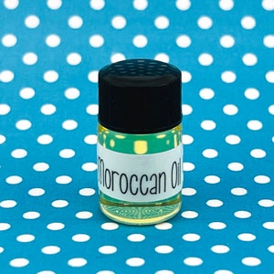 May include: A small, clear glass bottle with a black lid filled with a yellow liquid. The bottle has a white label that reads "Moroccan Oil".