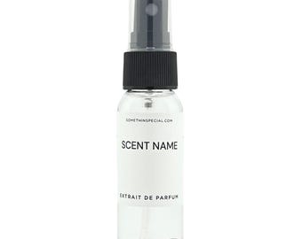 May include: A clear glass spray bottle with a black plastic cap and nozzle. A white rectangular label is centered on the bottle, featuring the text SOMETHINSPECIAL.COM, SCENT NAME, and EXTRAIT DE PARFUM in black, sans-serif capital letters.