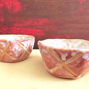 May include: Two small ceramic bowls with a white glaze and a textured, cross-hatch pattern. The bowls are a light orange color.