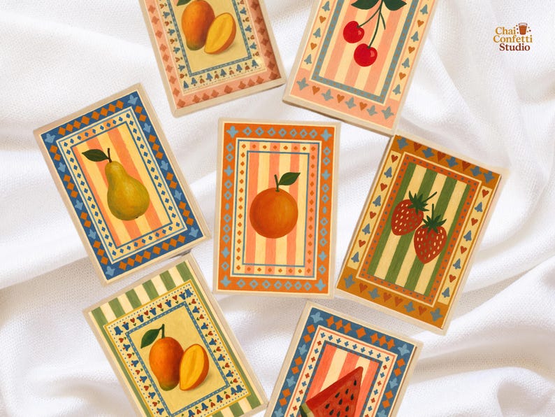 May include: A collection of rectangular cards with fruit illustrations. Each card features a different fruit, including mangoes, pears, cherries, oranges, strawberries, and watermelon. The cards have a striped background and decorative borders in various colors.