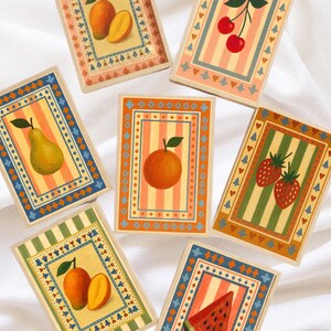 May include: A collection of rectangular cards featuring illustrations of various fruits, including pears, cherries, oranges, strawberries, mangoes, and watermelon. Each card has a striped background and decorative borders in shades of blue, orange, and green.