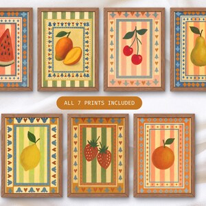 May include: Seven framed art prints featuring colorful illustrations of fruits, including a watermelon slice, mangoes, cherries, a pear, a lemon, strawberries, and an orange. Each print has a decorative border and a striped background.