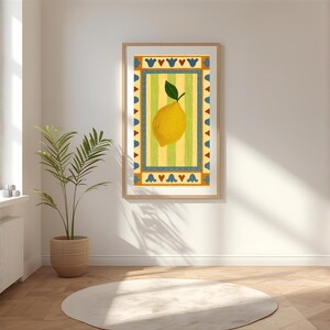 May include: A framed art print featuring a yellow lemon with a green leaf, set against a striped yellow and green background. The artwork is bordered by a decorative blue and orange pattern. The print is displayed in a bright, airy room with a plant and a round rug.