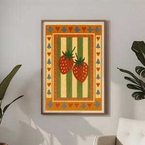 May include: A framed art print featuring two red strawberries with green stems on a striped background of yellow and green. The artwork has a border with hearts and tree-like shapes in orange, blue, and yellow. The print is in a wooden frame.