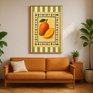 May include: A framed art print featuring a mango illustration. The artwork depicts a whole mango and a sliced mango against a yellow background with a decorative border. The frame is surrounded by a green and white striped pattern. The print hangs above an orange sofa.