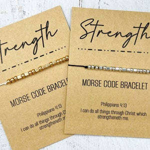 May include: Two cards with the word "Strength" written in black cursive. Each card has a black string bracelet with gold and silver beads that spell out "Strength" in Morse code. The cards include the Bible verse Philippians 4:13, "I can do all things through Christ which strengtheneth me."