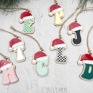Puede incluir: Ocho adornos navideños de madera con forma de letras con gorros de Papá Noel. Las letras son H, P, E, J, L, C, D y T. Cada letra está pintada en un color y un patrón diferente.