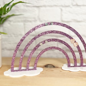 May include: A pink glitter rainbow earring holder with four tiers. The holder is sitting on a white cloud-shaped base.