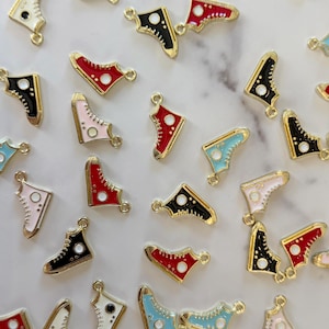 May include: A collection of colorful miniature sneaker charms in various colors, including red, black, pink, blue, and white. Each charm has a gold-colored outline and a small loop for attaching to jewelry or other crafts.
