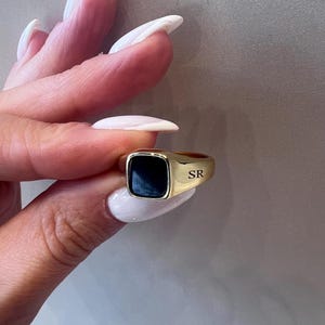 May include: Gold signet ring with a black square stone and the initials "SR" engraved on the side.