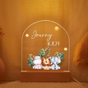 Może przedstawiać: Biała nocna lampka z akrylu z drewnianą podstawą. Lampka ma fantazyjny wzór z hipopotamem, lwem i słoniem otoczonymi zielonymi liśćmi. Na lampce nadrukowany jest tekst "Journey 16.11.24".