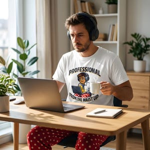 May include: A white t-shirt with the text "PROFESSIONAL FROM THE WAIST UP" and a cartoon graphic of a person working on a laptop. The person is wearing headphones and holding a white mug. The person is sitting at a wooden desk with a laptop.