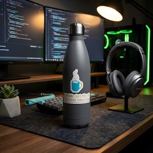 Puede incluir: Una botella de agua de metal gris mate con tapa plateada. La botella presenta una pegatina de arte píxel de una taza azul con vapor y una pegatina rectangular con el texto "//TODO: Let the AI fix this tomorrow" en fuente blanca.