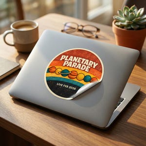 May include: A round sticker with a retro design featuring the words "PLANETARY PARADE" in white, with a colorful striped background. Below the text are illustrations of planets. The sticker also includes the text "LIVE FEB 2026".