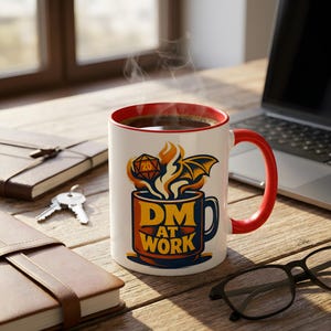 Puede incluir: Taza de cerámica blanca con interior y asa rojos, con el texto "DM AT WORK" en naranja y azul. La taza tiene un diseño de taza de café con un ala de dragón y un dado de 20 caras. Sale vapor de la taza.
