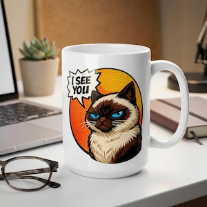 Op de afbeelding: Witte keramische mok met een illustratie van een chagrijnige kat met blauwe ogen en de tekst "I SEE YOU" in een tekstballon. De kat staat tegen een gele en oranje achtergrond.