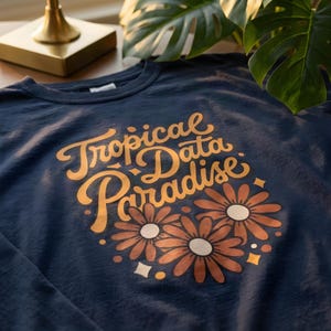 May include: A dark navy blue long-sleeve shirt featuring the text Tropical Data Paradise in a golden yellow script font. Below the text are three stylized flowers with brown petals and cream centers, accented by small golden yellow diamond and circle shapes.