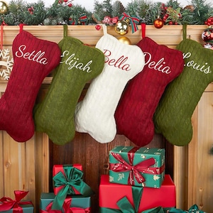 May include: Five Christmas stockings in red, green, and white hang above a fireplace. Each stocking is personalized with a name embroidered in a contrasting color. Presents wrapped in green and red paper with ribbons are stacked below.