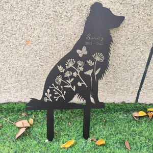 May include: Black metal dog silhouette garden stake with floral and butterfly details. The name "Sandy" and the years "2021-2023" are etched on the dog's body. The stake has two prongs for easy placement in the ground.