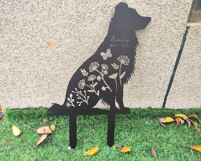 May include: Black metal dog silhouette garden stake with floral and butterfly details. The name "Sandy" and the years "2021-2023" are etched on the dog's body. The stake has two prongs for easy placement in the ground.
